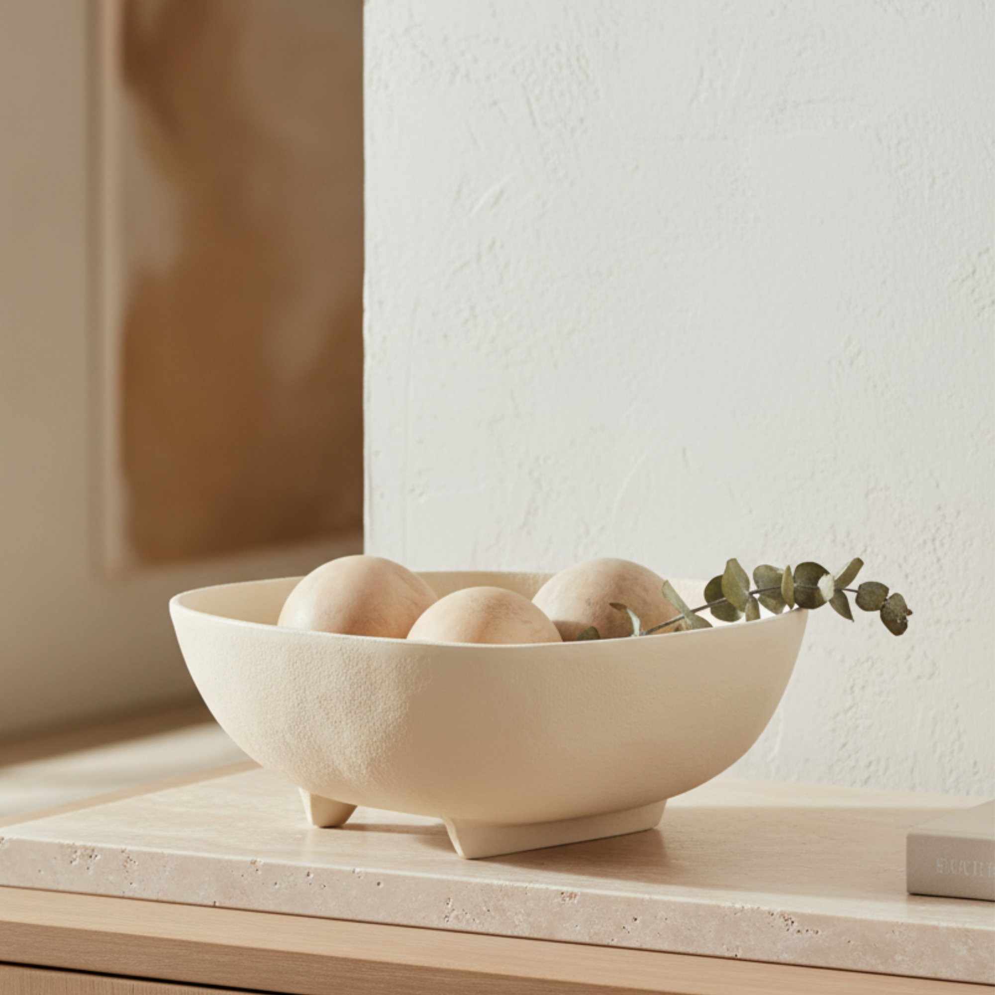 Beige ceramic bowl with eggs and a sprig of eucalyptus on a wooden surface.